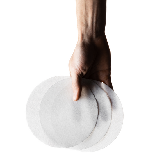 Hand holding flat paper filters against a white background